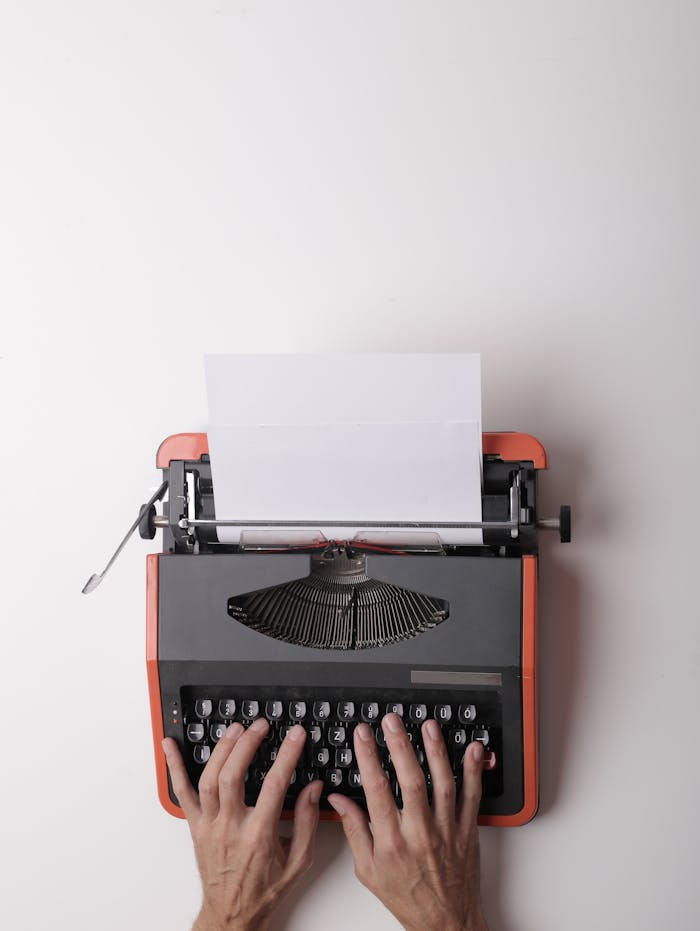 zipwp-image-3808904 From above crop person using vintage black and red typewriter with white blank sheet of paper against white background
